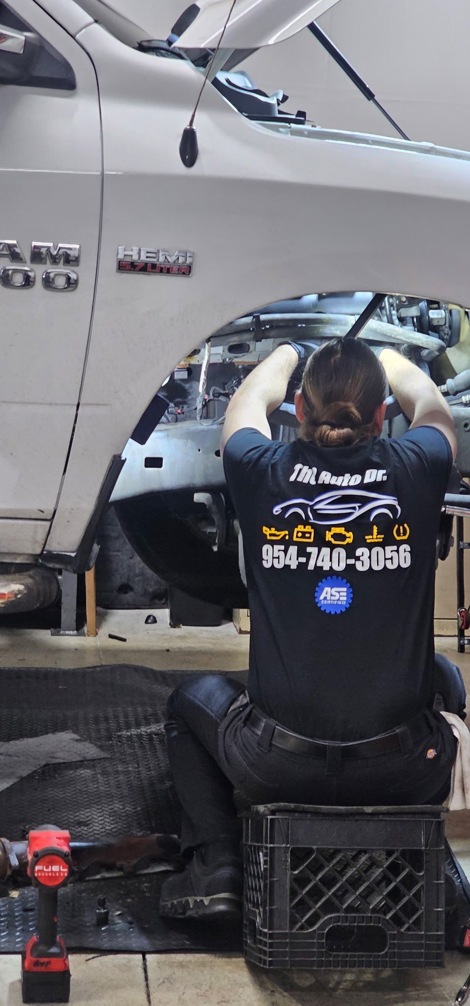 Mechanic working on engine bay of white GMC pickup truck with door open at repair shop